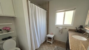 Ein Badezimmer mit Toilette, Duschvorhang, Waschbecken und einem kleinen Fenster.