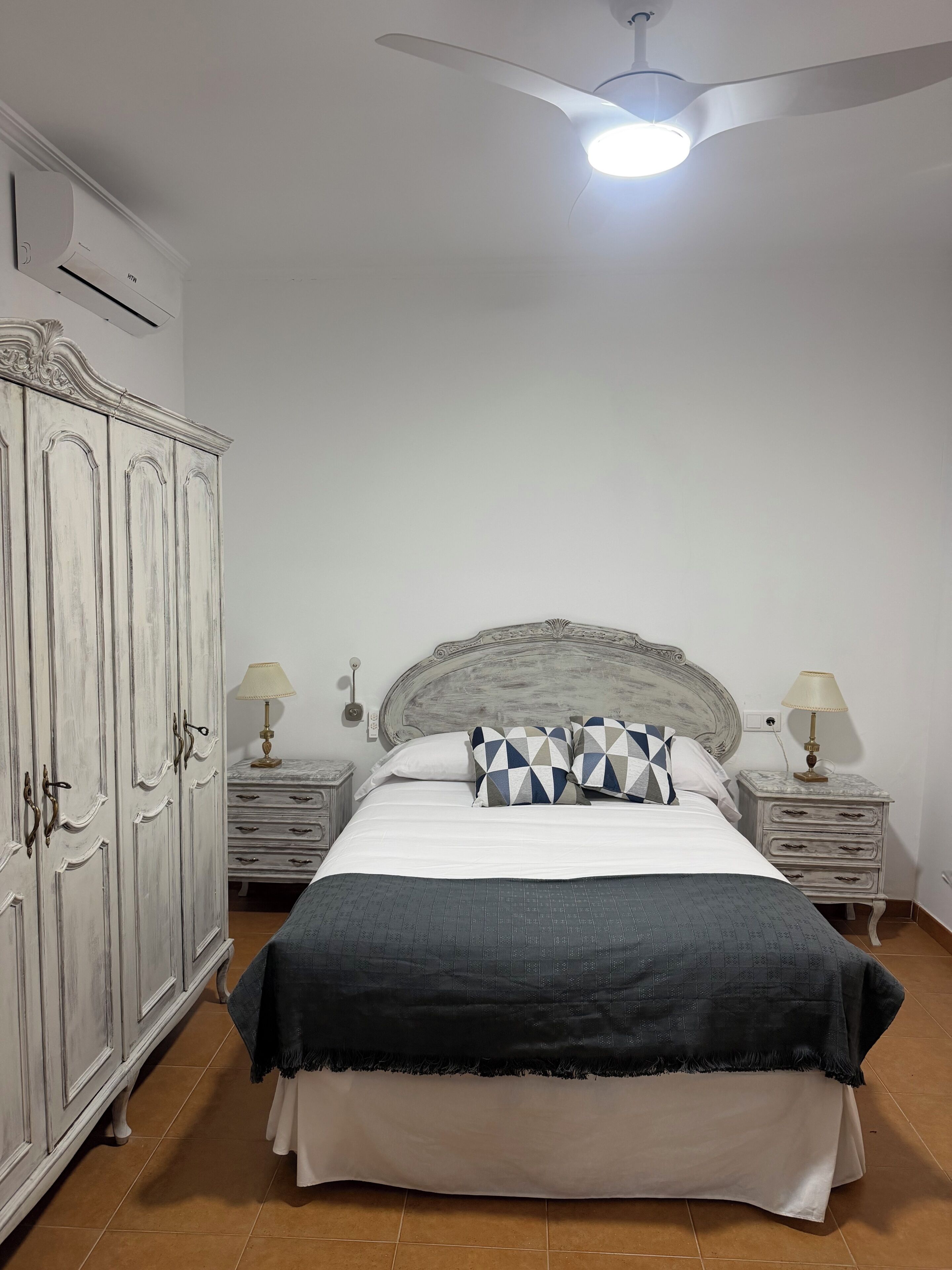 Ein Schlafzimmer mit einem Bett, zwei Nachttischen mit Lampen, einem Kleiderschrank und einem Deckenventilator.