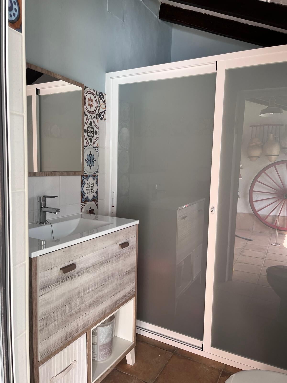Une salle de bain avec un meuble-lavabo blanc, un miroir, un espace douche et un mur carrelé.