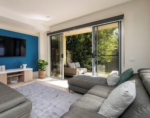 A modern living room with a grey sofa, a flat-screen TV, a coffee table, and a sliding glass door leading to an outdoor area. - Tides Edge in Capel Sound (Capel Sound)