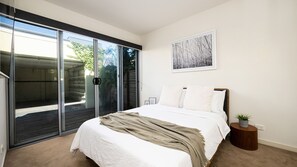 A bedroom with a bed, a sliding glass door, a framed picture, and a small round table with a plant.