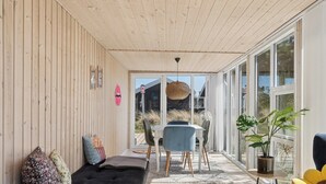 Un espace extérieur abrité, doté d’un plafond en bois, d’un canapé noir, d’une table à manger avec des chaises et d’une plante en pot.