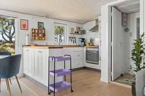 A modern kitchen with white cabinets, a wooden countertop, and a purple storage cart. - Holiday home in Vorupør near sea and nature (Thisted)