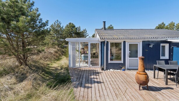 Une terrasse en bois, une porte vitrée, une table à manger et un grand vase.