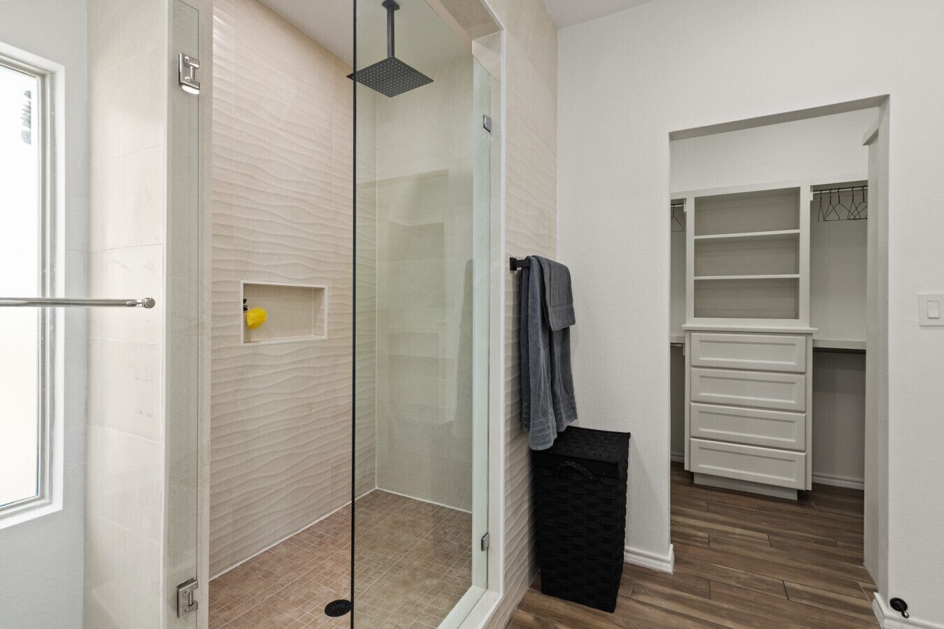 Un dressing avec des tiroirs et des étagères blancs, une cabine de douche en verre et un porte-serviettes.