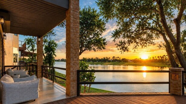 Terraza de madera con sofá y barandilla, con vista a un lago al atardecer.