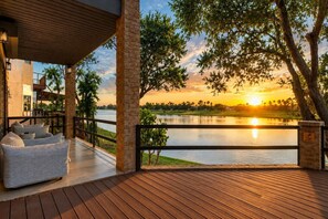 Une terrasse en bois avec un canapé et une balustrade, donnant sur un lac au coucher du soleil.
