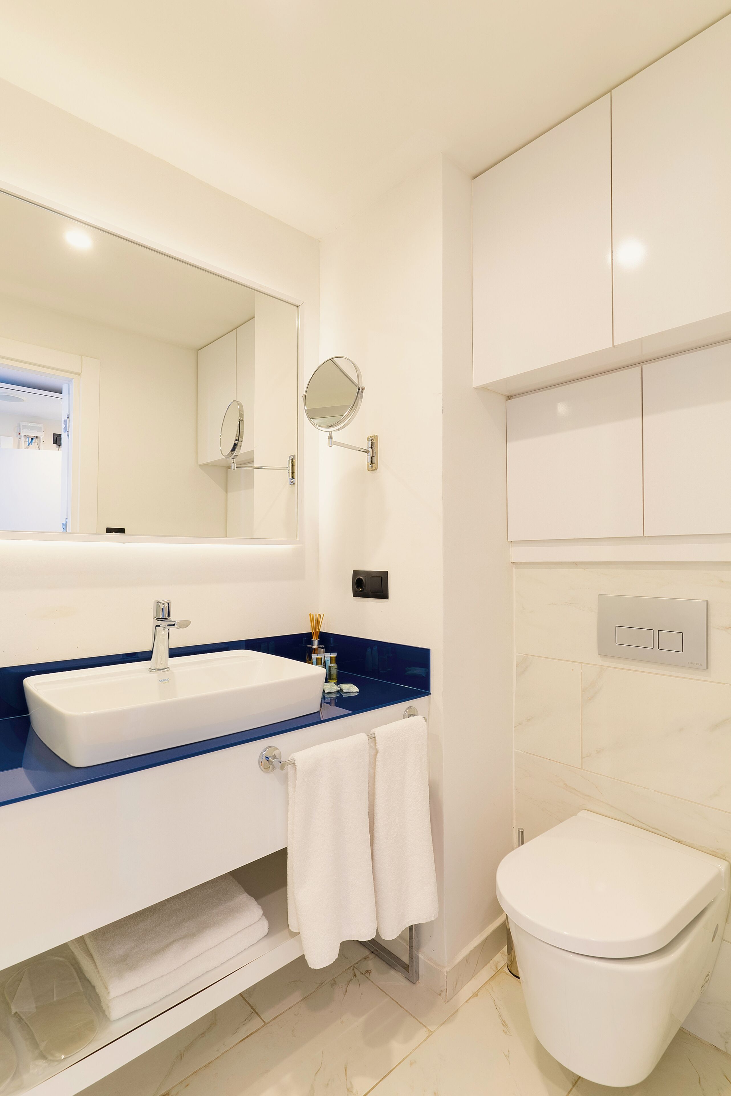 Ein modernes Badezimmer mit einem weißen Waschbecken, einer blauen Arbeitsplatte und einer weißen Toilette.