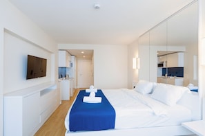 Ein modernes Hotelzimmer mit einem großen Bett, einem Flachbildfernseher, einem Schreibtisch und einem durch eine geöffnete Tür einsehbaren Badezimmer.