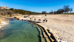 A river with clear water, a sandy beach, and a row of umbrellas and chairs. - Hill Country Family & Pickleball Retreat (Ingram)