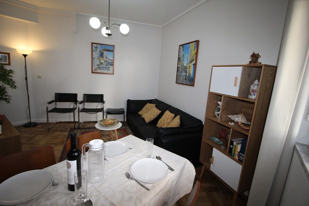 Un coin repas avec une table dressée pour deux personnes, un canapé en cuir noir, une bibliothèque et deux chaises.