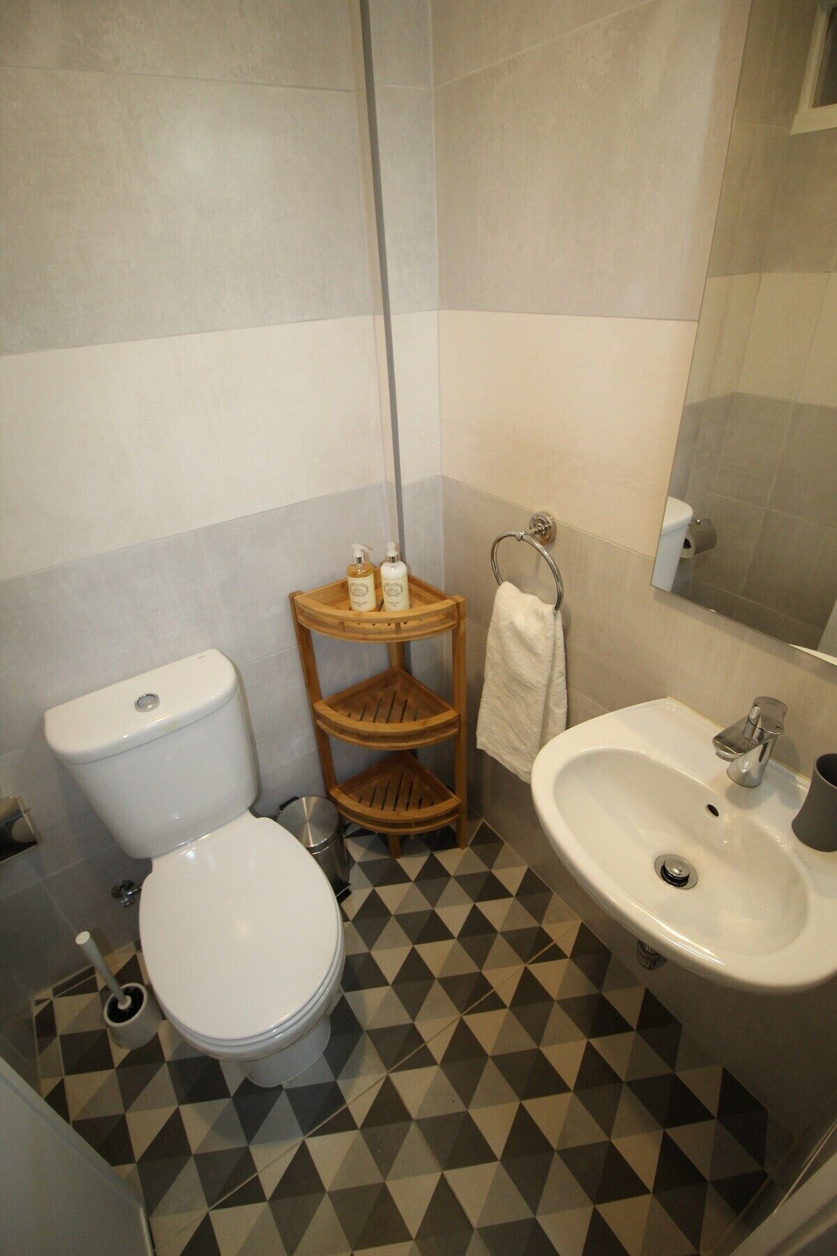 A bathroom with a toilet, sink, and a wooden shelf with toiletries.