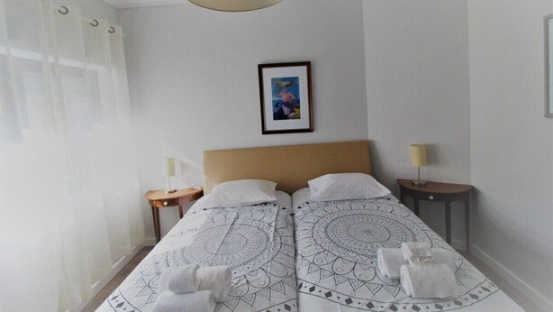 A double bed with patterned bedding, a framed picture on the wall, and two bedside tables with lamps. - Aveiro Apartment with Patio (Aveiro)