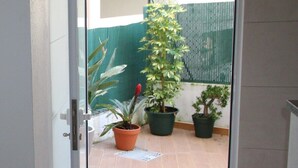 A door leading to a tiled patio with potted plants and a green fence. - Aveiro Apartment with Patio (Aveiro)