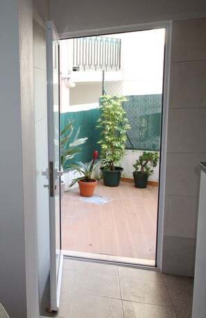 Eine Tür, die zu einer gefliesten Terrasse mit Topfpflanzen und einem grünen Zaun führt.