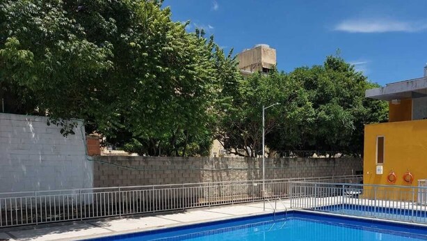 A rectangular swimming pool with a metal ladder, surrounded by a white tiled deck and a metal fence. - Comfortable apartment in Barranquilla, warmth of home, with pool, parking, gym and wifi. (Barranquilla)