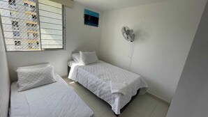 A room with two beds, a window with metal bars, a wall-mounted fan, and a small painting. - Comfortable apartment in Barranquilla, warmth of home, with pool, parking, gym and wifi. (Barranquilla)
