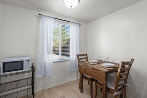 Ein Essbereich mit einem Holztisch, Stühlen, einer weißen Mikrowelle und einem Fenster mit Jalousien.