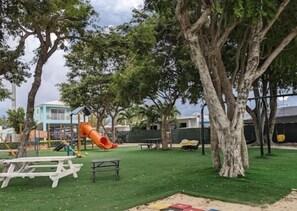 A playground with a slide and swings, surrounded by trees and a picnic table. - Key Largo 2BR Retreat | Pool & Boat Ramp (Key Largo)