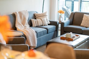 Un salon moderne avec un canapé gris, une table basse sur laquelle se trouve un plateau avec divers objets, et un vase rempli de fleurs.