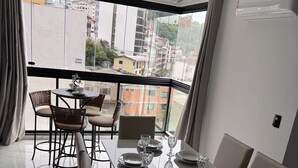 Ein Essbereich mit Tisch für vier Personen, ein Balkon mit Blick auf Gebäude und ein modernes Interieur.