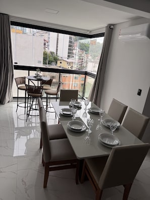 A dining area with a table set for four, a balcony with a view of buildings, and a modern interior design. - Apartment Flor de Romã - Villa Premium - 150m from the Thermal Park, Family-Friendly, Relaxing, Cozy (Piratuba)