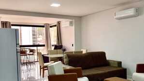 Ein modernes Wohnzimmer mit einer Couch, einem Hocker und einem Essbereich mit Stühlen und einem Tisch.