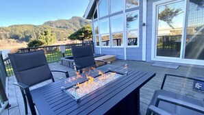Eine Terrasse mit Sitzgelegenheiten im Freien, einem Feuerbereich und Blick auf einen bewaldeten Hügel.