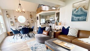 Ein modernes Wohnzimmer mit grauem Sofa, blauen und gemusterten Teppichen sowie einem Essbereich mit rundem Tisch und Stühlen.