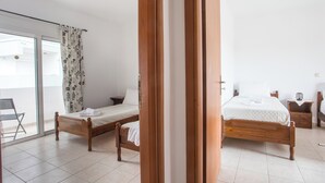 A bedroom with two wooden beds, a chair, a nightstand, and a sliding glass door leading to an outdoor area. - Ennisfree Villa (Kiotari)