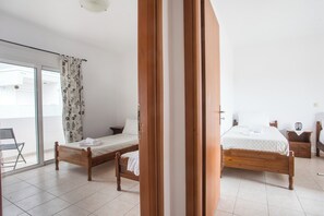 Una camera da letto con due letti di legno, una sedia, un comodino e una porta vetrata scorrevole che dà su uno spazio all'aperto.