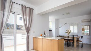 A modern kitchen with a central island, dining table, and chairs. - Ennisfree Villa (Kiotari)