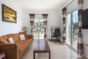 A living room with a sofa, a wooden table, a TV, and a sliding glass door leading to a balcony. - Ennisfree Villa (Kiotari)