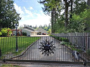 Ein verschlossenes Tor mit Sonnendesign, eine gepflasterte Auffahrt und ein Haus mit Garage und überdachter Veranda.