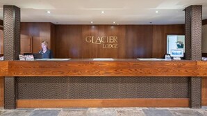 A reception desk at Glacier Lodge with a wooden finish, a receptionist, and a computer monitor. - 3BDR Luxury Ski-In&Out in|Prime Location|Valet Bike&Ski storage (Whistler)