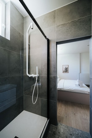 Un bagno moderno con doccia vetro, water e un letto nella stanza adiacente.