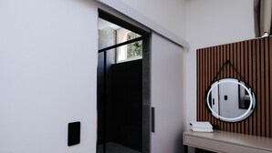 A modern bathroom with a wooden vanity, a round mirror, and a small stool.