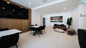 A modern hotel lobby with a dining area, seating, a large painting, and a sign indicating rooms.