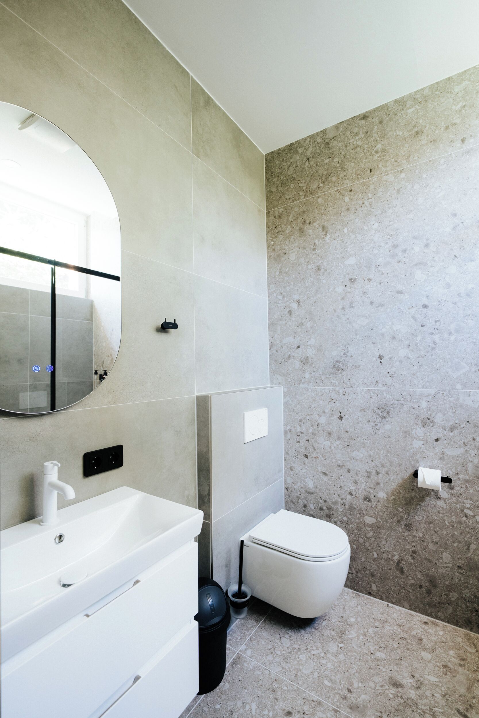 A bathroom with a white sink, mirror, and toilet, and a tiled wall.