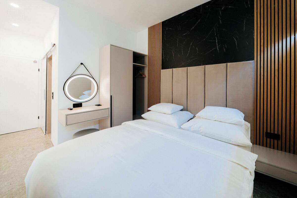 Ein modernes Schlafzimmer mit einem Bett, einem Nachttisch mit Spiegel, einem Kleiderschrank und einer Wand mit Schwarz-Weiß-Muster.