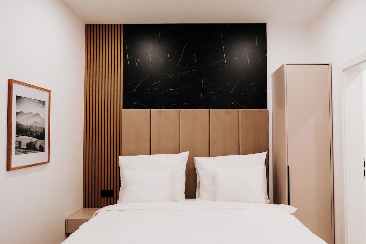 Ein modernes Hotelzimmer mit einem großen Bett, Holzvertäfelung, einem schwarzen Marmor-Kopfschild und einem gerahmten Bild an der Wand.