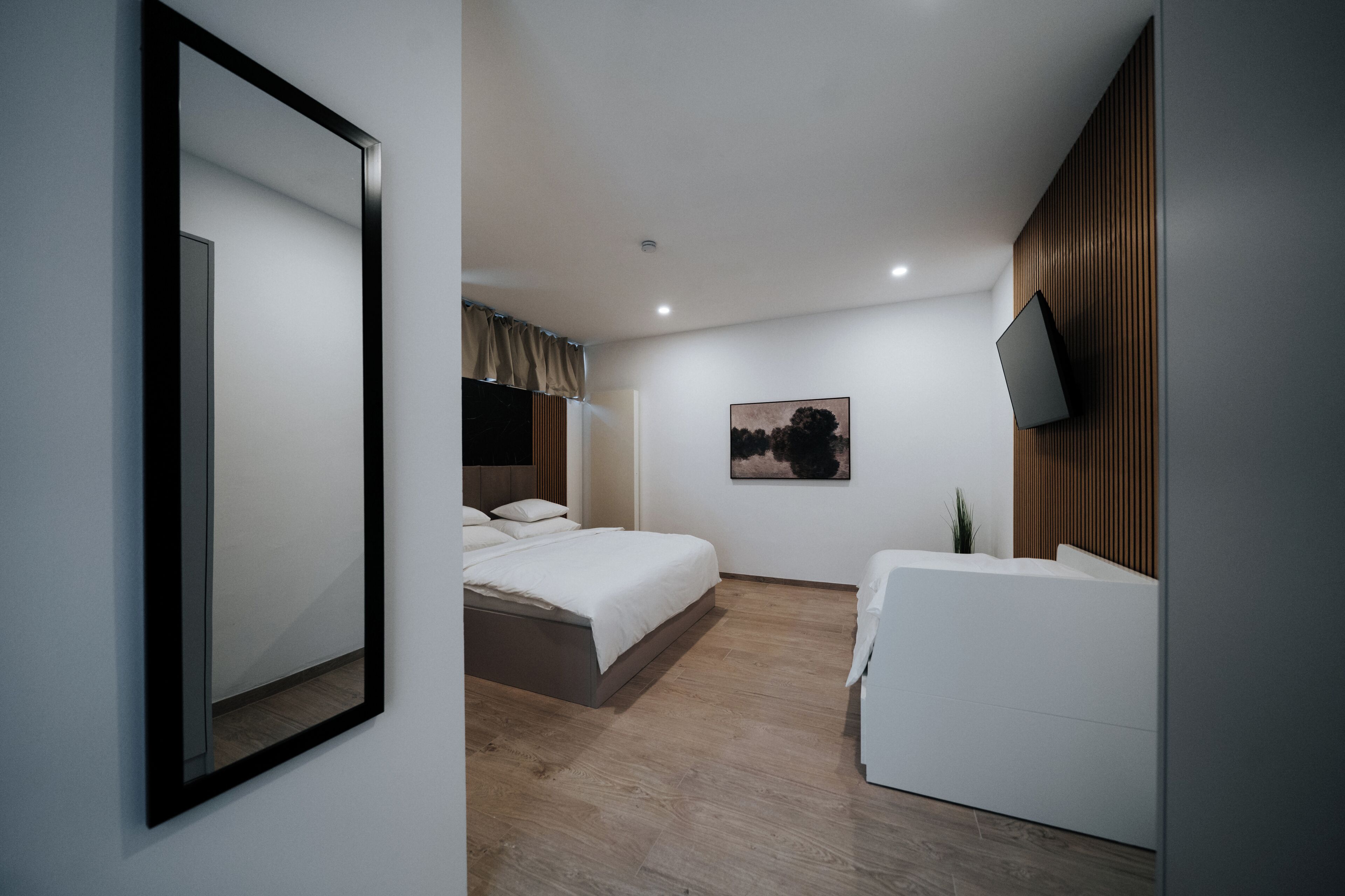 A modern hotel room with a large bed, a sofa, a flat-screen TV, and a painting on the wall.
