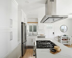A modern kitchen with white cabinetry, a stainless steel range hood, a gas stove, and a wooden island with a cutting board. - Coastal Manhattan Beach Home | Walk to Beach & Downtown (Manhattan Beach)