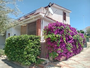 Ein Haus mit Satellitenschüssel, einem Backsteinsschornstein und einem großen Busch mit violetten Blüten.