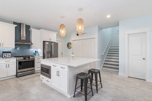 A modern kitchen with white cabinetry, stainless steel appliances, and a central island with stools.
