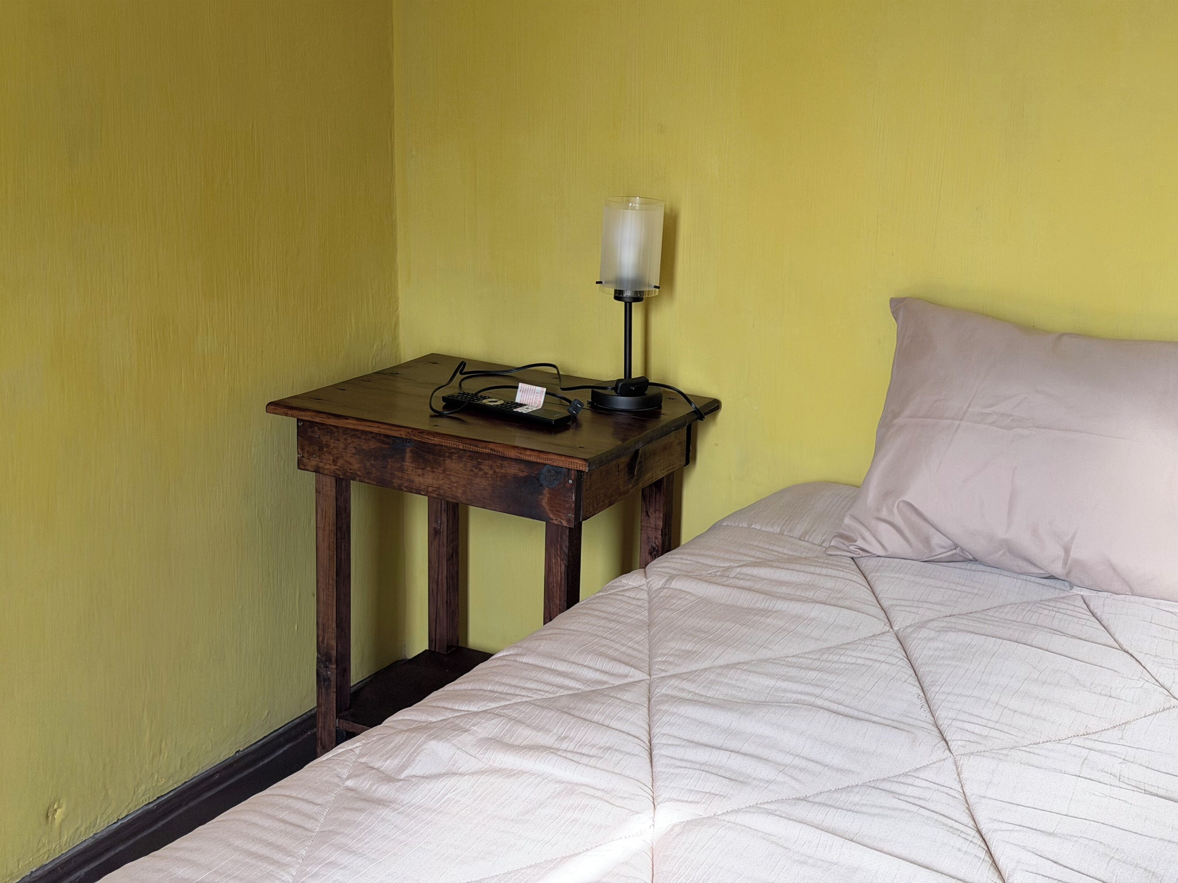 A bed with a quilted cover, a bedside table with a lamp, and a power strip.