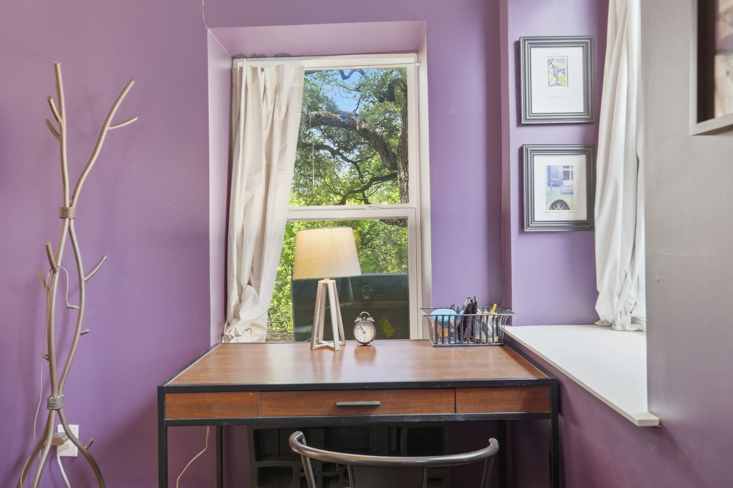 Een kamer met een bureau, een lamp, een klok en een raam met gordijnen.