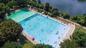 Oversigtsbillede af en stor, rektangulær swimmingpool omgivet af træer og en sø.