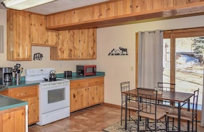 Une cuisine dotée de meubles en bois, d’une cuisinière, d’un four à micro-ondes et d’un coin repas avec des chaises et une table.