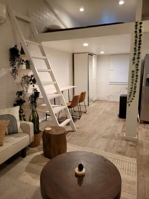 Un intérieur moderne avec un canapé blanc, une table basse en bois, une échelle blanche et un escalier menant à un niveau supérieur.